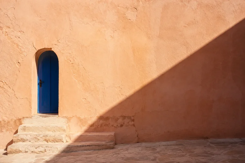 Afternoon shadows across terracotta walls and a cobalt doorway