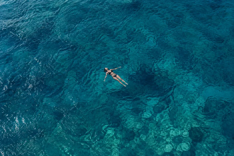 A swimmer floating in clear turquoise seawater, seen from above